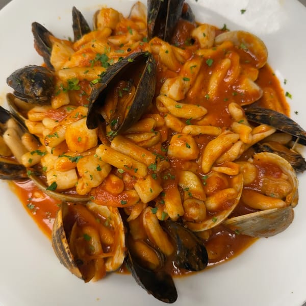 Seafood pasta with mussels, clams, and scallops in a rich red sauce, garnished with parsley.