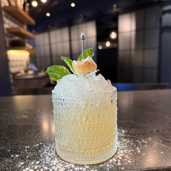 A cocktail with crushed ice, mint, and candied ginger in a textured glass on a dark bar.