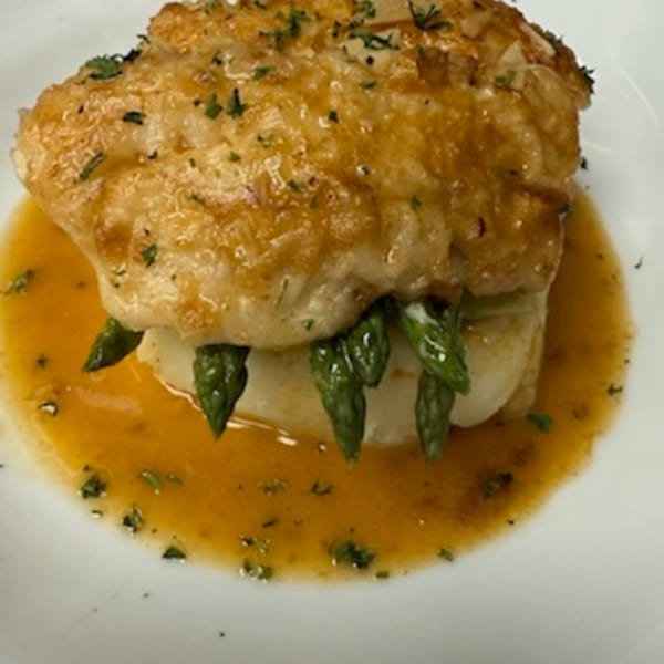 Golden-brown fish fillet with asparagus spears in a rich sauce, garnished with herbs.