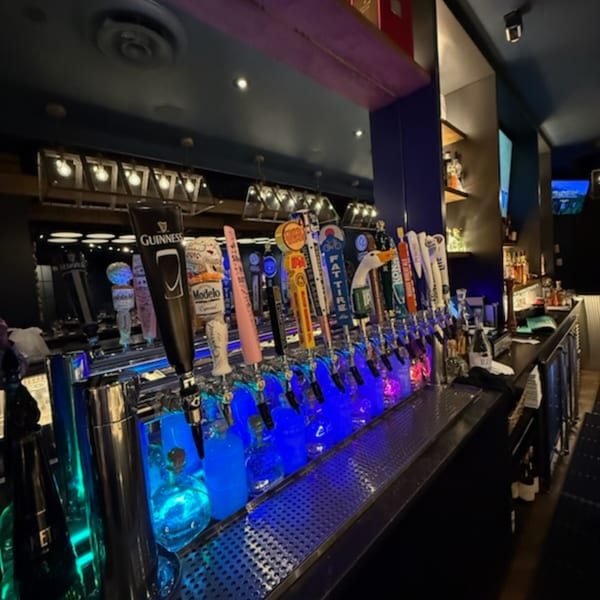 A long bar with many beer taps and glowing blue bottles, creating a vibrant atmosphere at Bar 141.