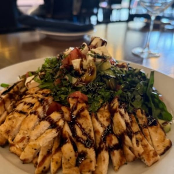 Grilled chicken strips with balsamic glaze, fresh greens, tomatoes, and mozzarella on a white plate.