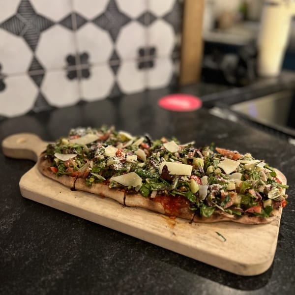 Bar 141's flatbread pizza, topped with fresh greens, tomatoes, and shaved parmesan, on a wooden board.
