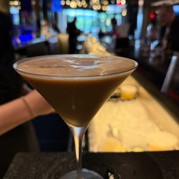 A martini glass filled with a creamy brown cocktail sits on a bar counter at Bar 141.