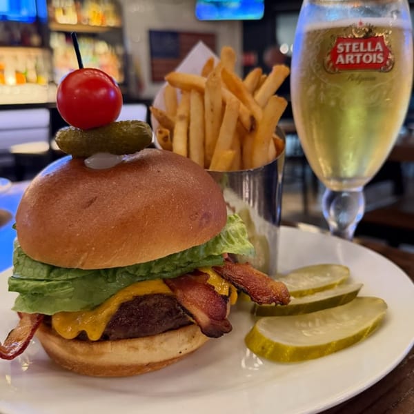 Bacon cheeseburger with fries, pickles, and a Stella Artois beer at Bar 141.