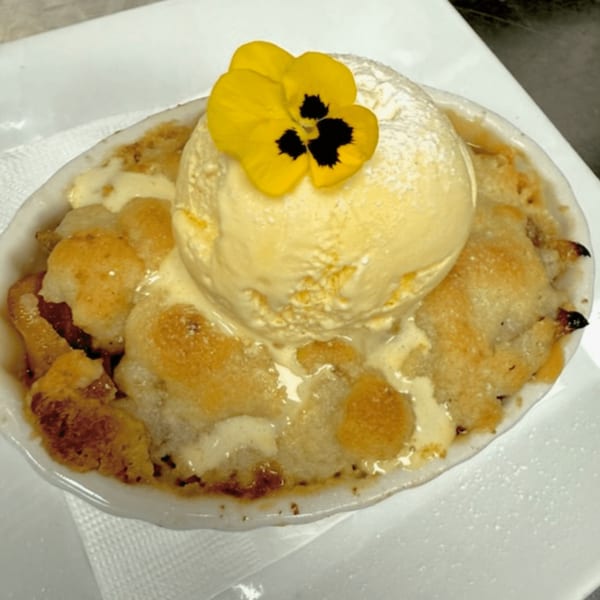 Warm fruit crumble with a scoop of vanilla ice cream and a yellow edible flower.