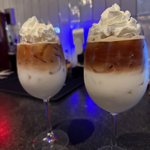 Two iced coffee drinks with whipped cream in wine glasses on a bar counter with blue lighting.