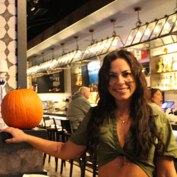 A smiling woman with long dark hair poses next to a pumpkin inside Bar 141.