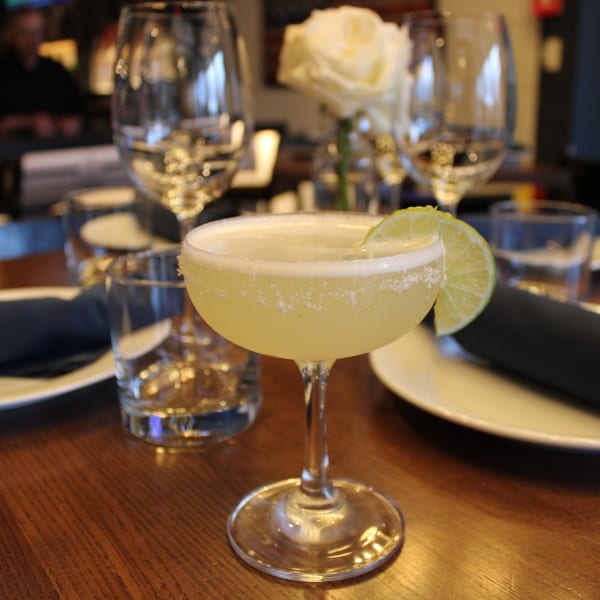 A Bar 141 cocktail, garnished with a lime wedge and salt rim, on a wooden table.